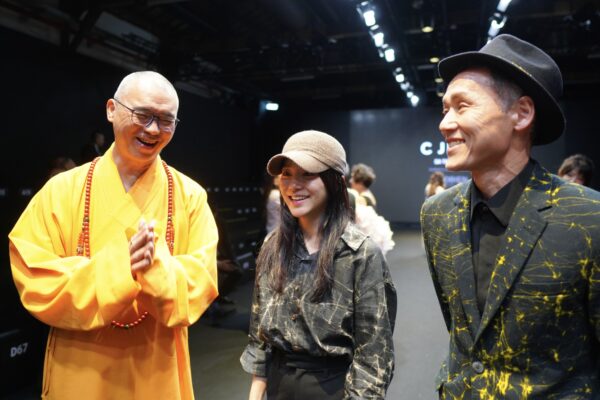 C JEAN 於文化部主辦26AW 臺北時裝週開幕秀現場，圖中合影除模特兒外，唯一女性為品牌設計師簡君媛；首秀焦點模特兒手持之經書， 國立故宮博物院與僧伽林文化出版有限公司合作之國寶復刻文創「普門品」。圖/楠西萬佛寺
